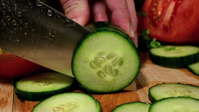 man with chef's knife slicing a cucumber on wooden board