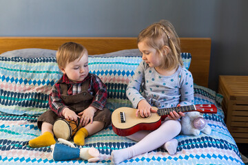 Horizontal view of adorable happy blond baby boy sitting on bed looking at his older cousin...