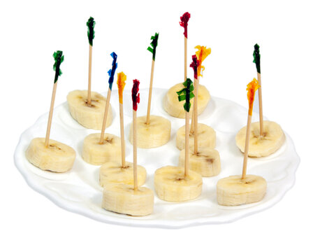 Banana slices appetizer on a white plate with color-topped cellophane toothpicks. 