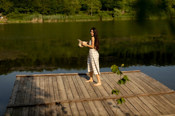 Fototapeta na wymiar Young woman standing on the wooden pier at the calm lake