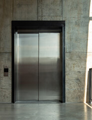 Elevator chrome metal with closed door on Bare cement wall for lifting people to the upper floors with push switch for up and down at modern building design. Selective focus.