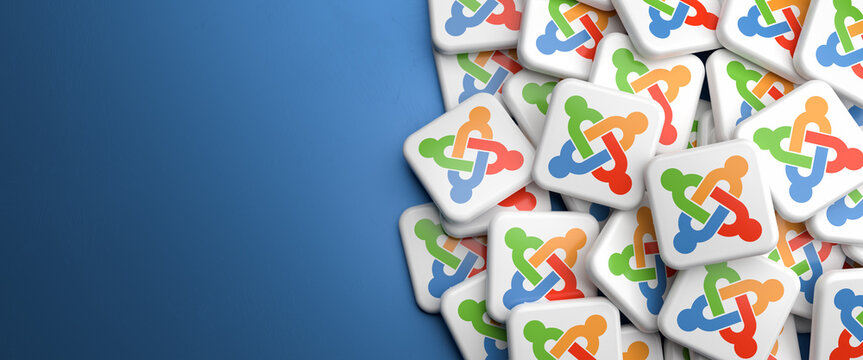 Logos of the Web Content Management System Joomla! on a heap on a table. Copy space. Web banner format.