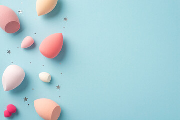 Make up concept. Top view photo of different colour beauty blenders and star shaped confetti on isolated pastel blue background with copyspace