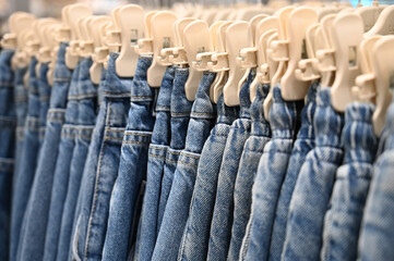 Denim jeans store detail. Row of blue jeans hung on plastic hangers in store. Many jeans are hanging on counter.