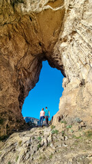 Hiking Couple standing in hole of rock formation Montepertuso Il Buco on hiking trail Path of Gods...