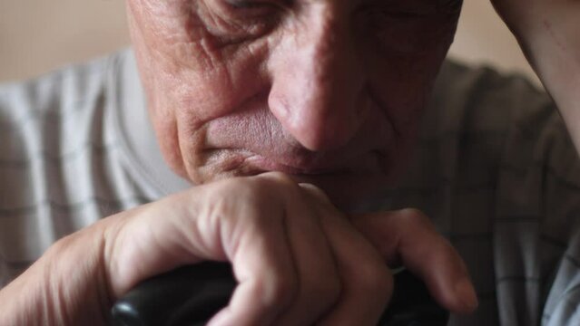 Close-up portrait of caucasian sad pensioner 70 years old sitting meditating with walking stick. Slow motion. The theme is the elderly. Selective focus