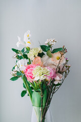beautiful bouquet of carnations, daffodils, spray roses, Chamelacium hookata and white irises on gray background, copy space
