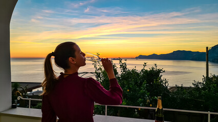 Woman with champagne glass in dress with scenic sea view at sunset from luxury apartment on...