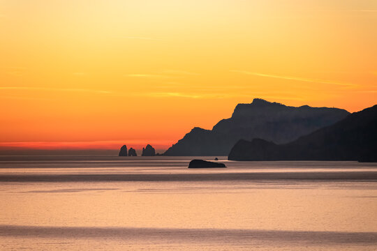 Panoramic sunset view from Praiano at Mediterranean Sea, Italy, Campania, Europe. Silhouette of Li Galli islands and coastline of Amalfi Coast. Reflection of sun beams on water surface during twilight