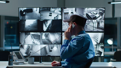 Security officer answer phone call watching cctv cameras on multi-screen workstation 