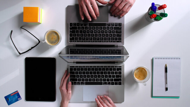 Top view of colleagues work together and type on laptop sitting at desk