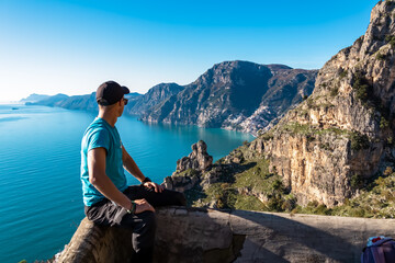 Man with panoramic view from hiking trail Path of Gods between coastal towns Positano and Praiano. Trekking in Lattari Mountains, Apennines, Amalfi Coast, Campania, Italy, Europe. Mediterranean Sea