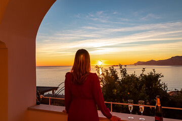 Woman with champagne glass in dress with scenic sea view at sunset from luxury apartment on Mediterranean Sea. Terrace balcony with arch at coastline in Praiano, Amalfi Coast, Campania, Italy, Europe © Chris