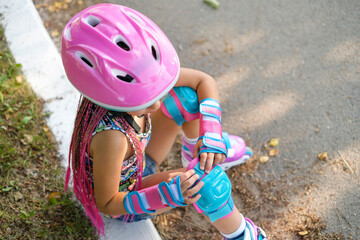 A child wearing a helmet puts on protective knee pads from falls for roller skating on city tracks.