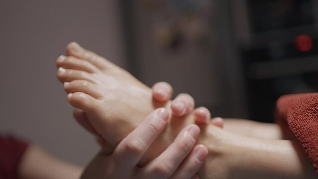 Close-up of masseur massaging legs. Action. Masseur's hands crumple client's beautiful feet. Gentle foot massage with oils in spa