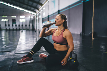 Side view of Caucasian female in activewear drinking water from bottle refreshing during sportive...
