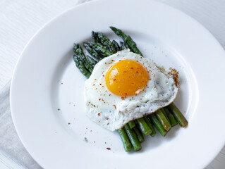 Cooking asparagus. Fried asparagus sprouts and fried eggs on a white plate. Healthy food and diet.