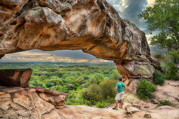 A man under the rock arch on Cerro Arco in Tobati in Paraguay. - obrazy, fototapety, plakaty