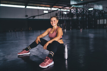 Fototapeta na wymiar Portrait of happy female athlete taking rest during daytime for workout practice, cheerful fit girl in active tracksuit smiling at camera feeling good from well done training in sportive gym studio