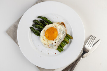 Cooking asparagus. Fried asparagus sprouts and fried eggs on a white plate. Healthy food and diet.