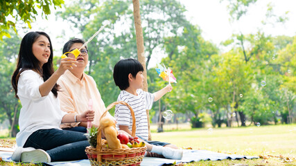Asian family enjoys a picnic in the garden during their vacation. Grandma, mother and son relax in...