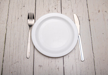 A empty plain white plate and cutlery with signs of use on a rustic wooden surface