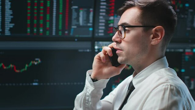Stock market broker talking on mobile phone with graphs on multiple computer screens at background