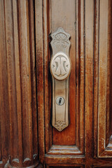 Old metal knob on a solid brown wooden door with a lock