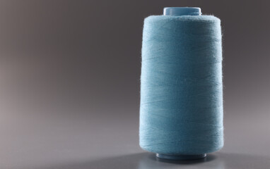 Fototapeta na wymiar Blue colour thread spool on grey background, thread for dressmaking industry, yarn for sewing