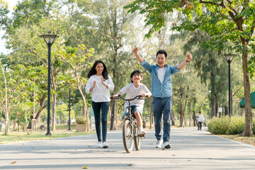Happy Asian father and mother teach their son to ride a bicycle, Cheerful parent raise hands up in...