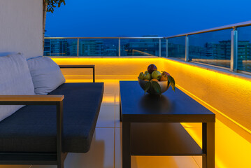 View of a cozy outdoor terrace with an armchair and a coffee table, LED lighting in the evening.
