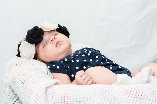 beautiful latina baby girl resting on a white sheet, dressed in a blue romper suit, white stockings and a black and white flower headband. maternity concept