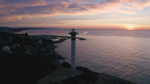Ellipse-shaped drone shot around a lighthouse at sunrise.