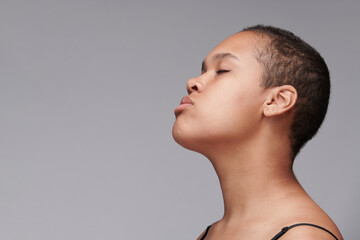 Side view of calm young black woman with buzz cut keeping eyes closed against gray isolated...