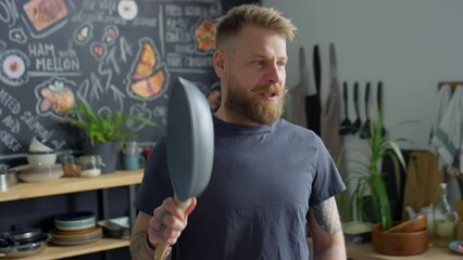 Cheerful food blogger telling about frying pan on camera while filming vlog in kitchen