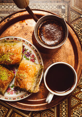 Still life with hot oriental coffee brewed in cezve. On the Arabic table is a small coffee cup and delicious honey baklava with pistachios on a saucer. View from above