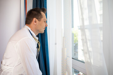 Pensive young male Caucasian doctor in white medical uniform look in window distance thinking or pondering, serious man GP plan future career or success in medicine, visualize at workplace