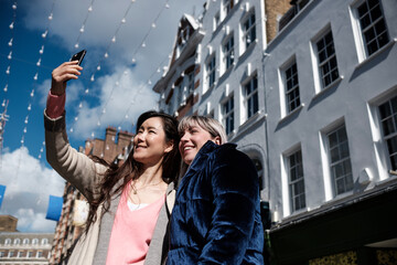 Multiracial mature women friends making a selfie in a London street.