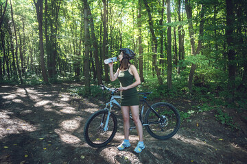 Fitness girl wear green dress rides a modern mountain bike in forest at hot summer day