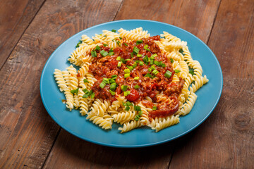 Blue plate with bolognese pasta on a wooden table sprinkled with onions.