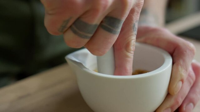 Close up shot of hands of male chef grinding toasted sesame seeds with mortar and pestle while preparing paste