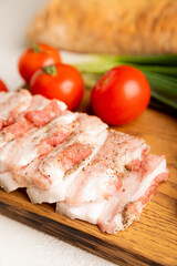 Board with pork fat, green onions, homemade bread and cherry tomatoes on a gray stone background....