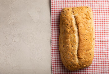 Fresh homemade bread on a kitchen towel on a gray cement background. Bread with flax seeds, sunflower seeds and sourdough bran. Organic homemade baked goods. Place to copy.