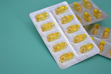 Blisters with yellow Omega 3 capsules on a colored background close-up. Fish oil, dietary supplement, vitamins, amino acids, medicine, health.