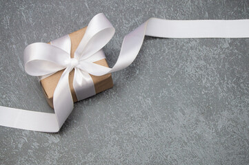 A gift box in craft paper with a white ribbon lies on a dark textured background. A postcard with a place for the text. Top view