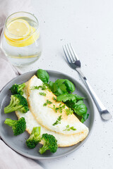 Protein omelet with broccoli and greens on a gray plate with lemonade on a gray background.Healthy food concept.