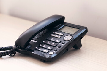 Black office phone on the wooden table. Communication technology concept.