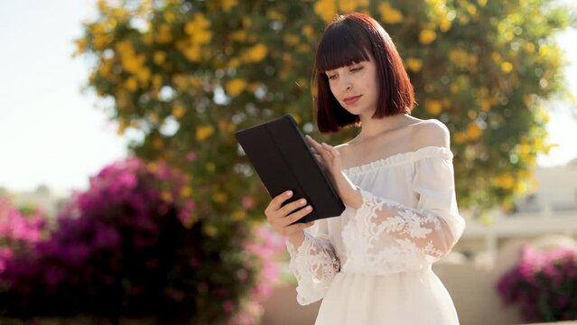Happy traveling woman on white dress and straw hat using tablet reading news on the Internet using wifi in exotic hotel. Woman working on the digital tablet