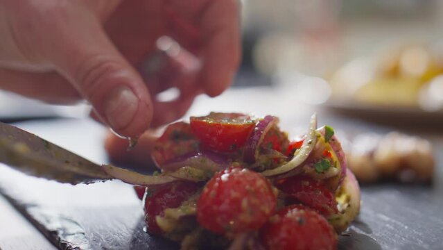 Close up shot of hands of chef putting tomato salad on black wooden board with spoon as side dish