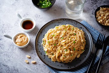 Wheat pasta with peanut butter soy sauce, roasted peanuts and scallion in a plate